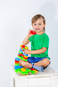 小男孩玩许多五颜六色的塑料积木室内构造器