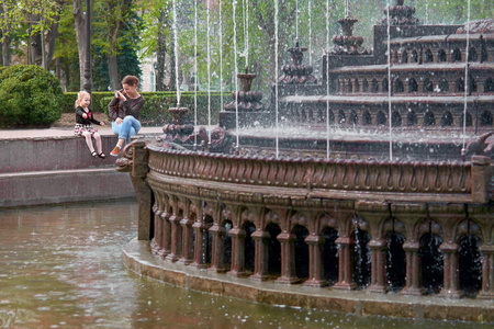 小女孩与一个女母亲在喷泉与照片, 在喷泉附近玩