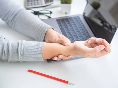 特写女人抱着她的手腕疼痛从使用电脑时间太长。办公室综合征概念