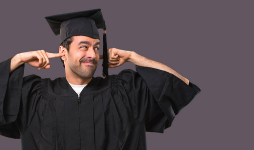 人在他的毕业天大学覆盖了两个耳朵用手在紫罗兰色背景