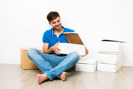 穿着蓝色衬衣的年轻人坐在 cardbox 旁边的地板上, mooving 去新房。在白色背景上