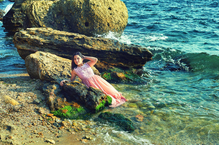 穿着粉红色连衣裙的年轻女孩在水中。在海滩上休息的女孩