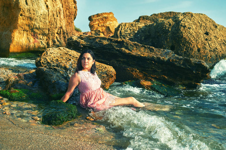 穿着粉红色连衣裙的年轻女孩在水中。在海滩上休息的女孩