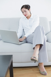 一个衣着光鲜的女人在沙发上使用笔记本电脑的全长