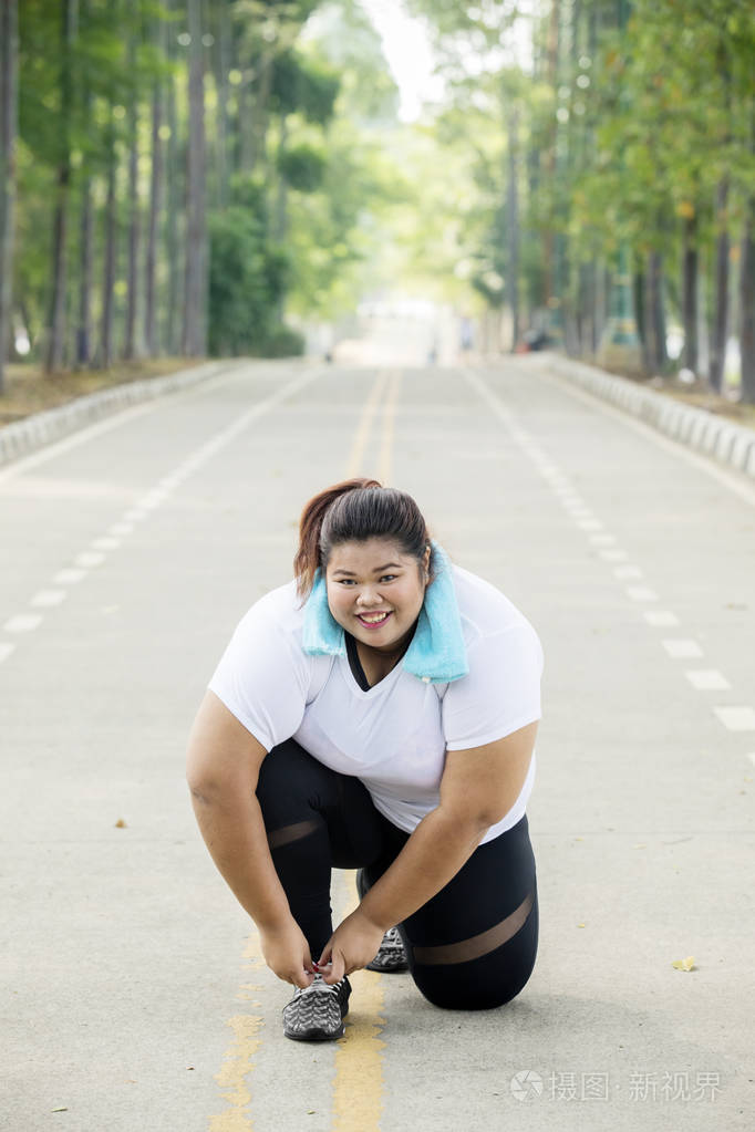 照片的胖女人微笑着在相机 而绑鞋带的道路上
