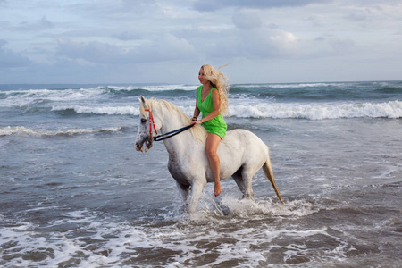 的年轻女子步行与马在沙滩上, 马背上