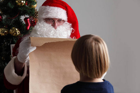 圣诞老人与与名单或尼斯或 naugthy 名单纸与小男孩在圣诞节树附近