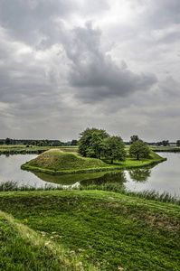 从 Leusden 的设防镇的城墙看, 荷兰对一个戏剧性的天空下的护城河附近的岛屿