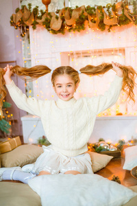 可爱的小女孩与金发长卷发在一个光针织毛衣由节日壁炉与花环和蜡烛