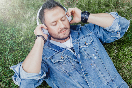 关闭的人躺在绿草和听音乐的耳机