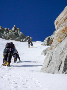 三个登山者在陡峭的北面上, 朝一个狭窄的库洛尔驶去