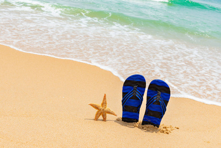 一双拖鞋和一只海星在海滩前面波浪来临