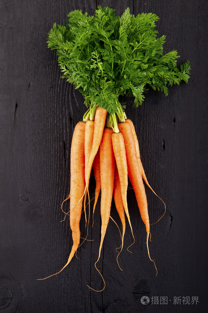 束新鲜胡萝卜与绿色叶子在木制的背景