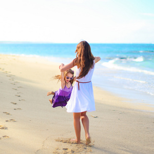 年轻的快乐妈妈和可爱的女儿在异国风情的沙滩上阳光明媚的日子开心