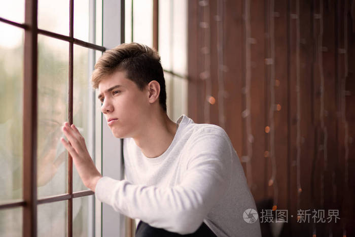 一个英俊的年轻人望着窗外的肖像.悲伤的少年16-18