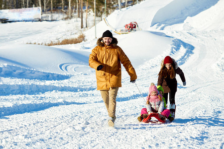 白种人拖着雪橇, 小孩子沿雪路在寒冷晴朗的日子, 他的妻子走在他们身后