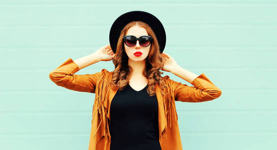 时尚肖像年轻妇女在黑色圆帽子, 太阳眼镜摆在灰色墙壁背景