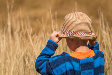 站在一片黄草地前的小男孩戴草帽照片
