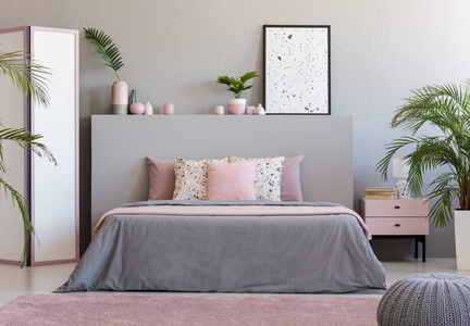 在灰色和粉红色卧室的灰色床头板上的海报与植物。真实照片