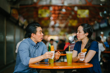 一个好看的中国亚裔夫妇的肖像在周末在新加坡, 亚洲享受小吃在小贩中心。他们正在享受汁和油炸香蕉