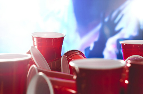 许多红色党杯子以模糊的庆祝人在背景。大学酒精容器在混合的位置。市场推广活动或啤酒乒乓球锦标赛