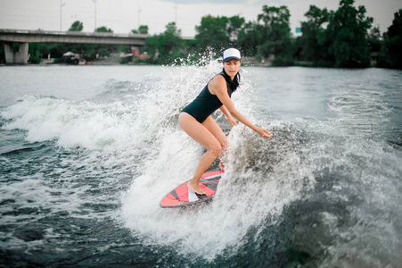 年轻活跃的黑发女孩骑在 wakesurf 的背景下的摩托艇高浪