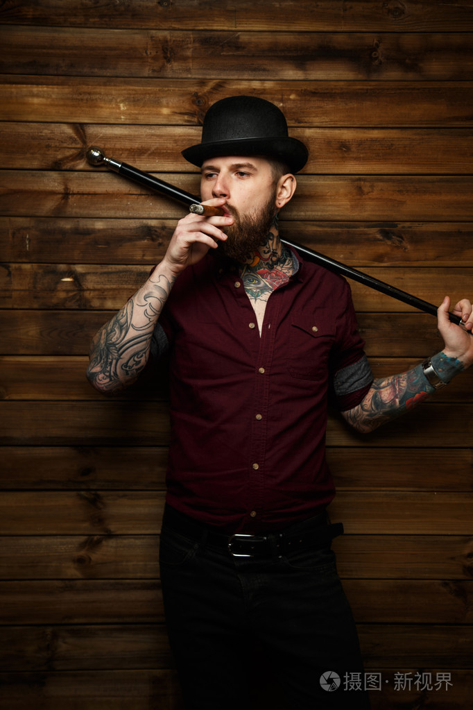 纹身的男人抽烟和持有手杖
