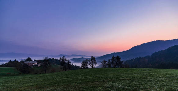 雾黎明在山和山谷在斯洛文尼亚莱夫库拉斯。紫色的天空。圣托马教堂