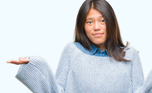 年轻的亚洲妇女穿着冬季毛衣在孤立的背景下无能和混淆表达与手臂和手提出。怀疑概念