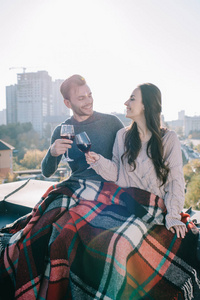 幸福的年轻夫妇覆盖格子和在屋顶上喝红酒