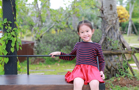 愉快的亚洲小女孩坐在公共花园的木长凳上