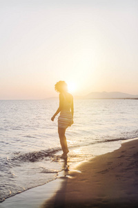 美丽的女人站在沙滩上享受日落