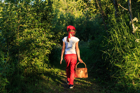年轻女孩走在一条小路上, 穿过绿色的树林背着篮子