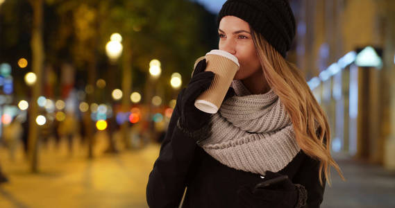 迷人的女人在城市环境中喝咖啡在晚上