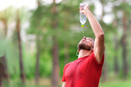 健身男子从瓶子里喝水。口渴的运动员在剧烈运动后喝冷饮