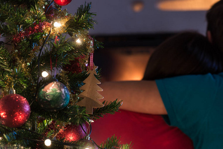 特写镜头装饰圣诞树与假日灯和年轻夫妇坐在壁炉拥抱