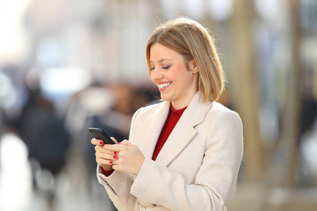 在冬天站在街上的快乐女人使用智能手机