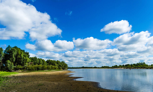 一条宽阔的河流沿着对角河岸流淌, 森林下有一片美丽的蓝天, 在水中