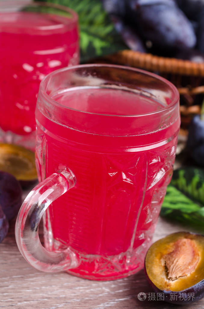 红色饮料在玻璃与新鲜李子在木制背景.选择性对焦