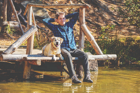 那个带着拉布拉多猎犬的人坐在湖岸的木甲板上。享受生活的人