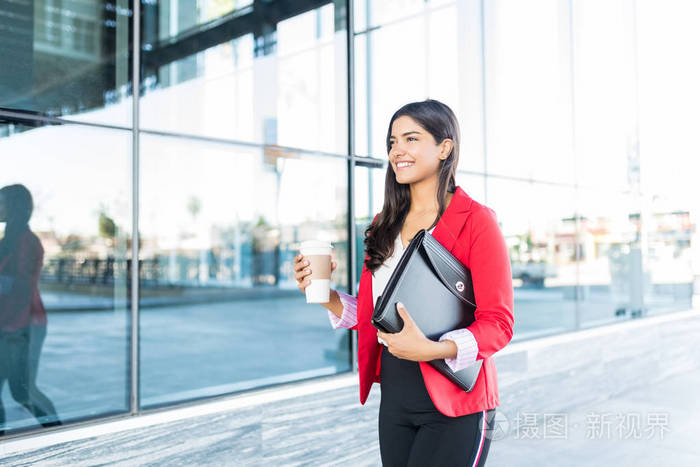 微笑的年轻女子与一次性咖啡杯和文件夹步行在办公楼