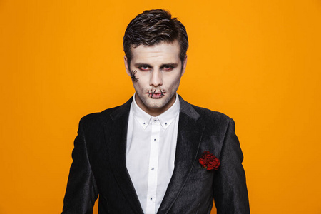 严重的僵尸新郎在正式西装和万圣节化妆看相机孤立在橙色照片