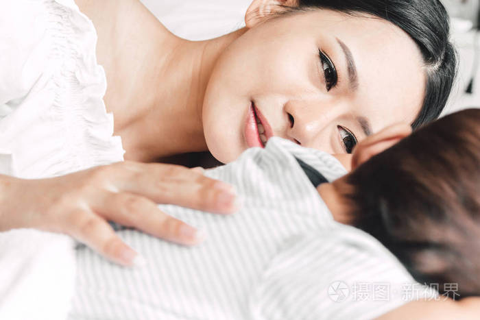 母亲抱着熟睡的婴儿手在白床上.对家庭概念的爱