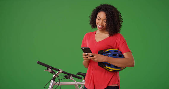 美丽的微笑的黑人女孩使用手机站在旁边的自行车在绿色屏幕上