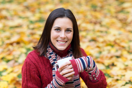 秋天公园里有一杯茶的年轻微笑的女人