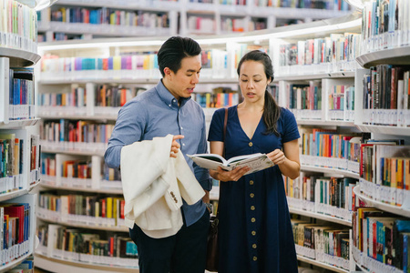 一对中国亚洲夫妇正在约会。周末他们正在图书馆看书。当他们站得很近的时候, 他们面带微笑