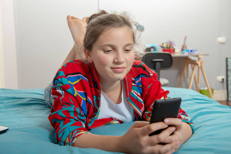一个十几岁的女孩躺在床上, 使用智能手机