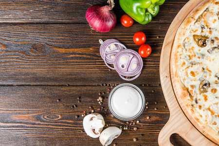 食品背景设计。白色酱汁, 洋葱, 蘑菇, 比萨饼在一个黑暗的木制背景。成分