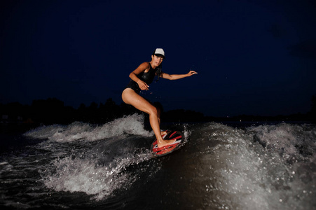 年轻迷人的黑发女子骑上橙色 wakesurf 在高空摩托艇上的夜空背景下