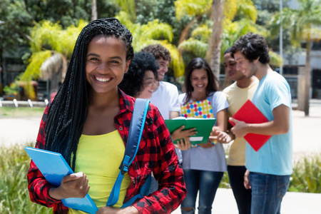 聪明的非洲裔美国女学生与一群学生户外在大学校园在夏天
